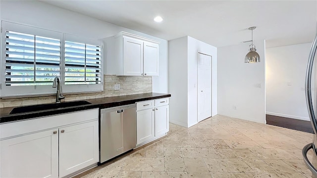 kitchen featuring tasteful backsplash, dark countertops, stainless steel dishwasher, white cabinetry, and a sink