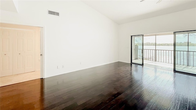 empty room with high vaulted ceiling, dark wood-type flooring, and visible vents