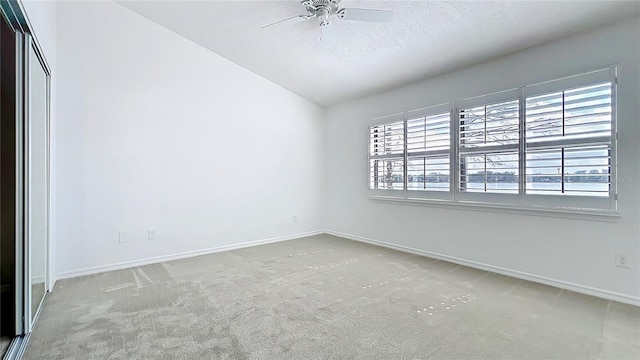 carpeted empty room featuring ceiling fan, vaulted ceiling, plenty of natural light, and baseboards