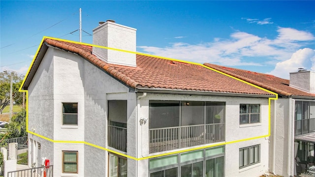 view of side of property with a tiled roof, a chimney, fence, and stucco siding