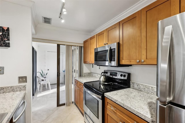 kitchen with appliances with stainless steel finishes, ornamental molding, light tile patterned floors, light stone counters, and track lighting