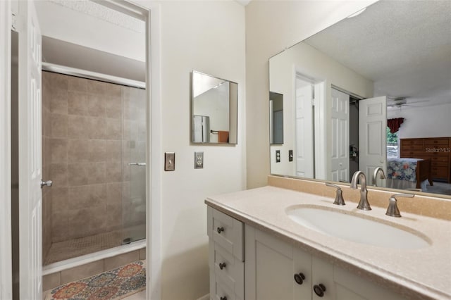 bathroom with ceiling fan, vanity, an enclosed shower, and a textured ceiling