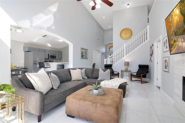 living room with ceiling fan, a towering ceiling, and a fireplace