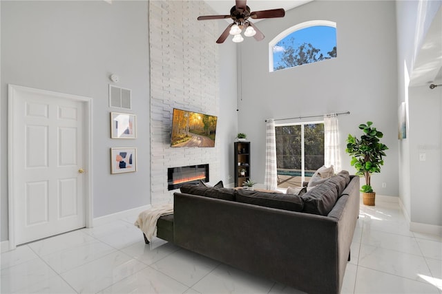 living room with a high ceiling, a large fireplace, and ceiling fan