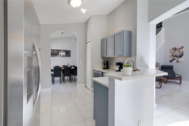 kitchen with a towering ceiling, gray cabinetry, decorative backsplash, kitchen peninsula, and stainless steel refrigerator with ice dispenser