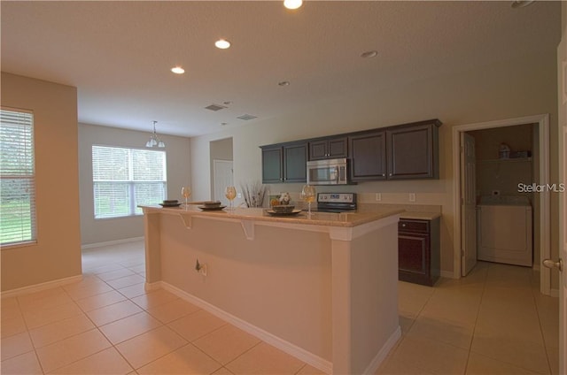 kitchen with a kitchen bar, a center island with sink, stainless steel appliances, light tile patterned flooring, and washer / clothes dryer