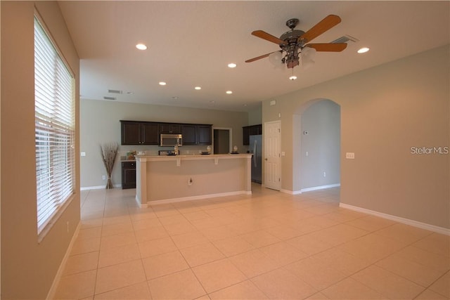 kitchen featuring dark brown cabinetry, a breakfast bar area, an island with sink, ceiling fan, and stainless steel appliances