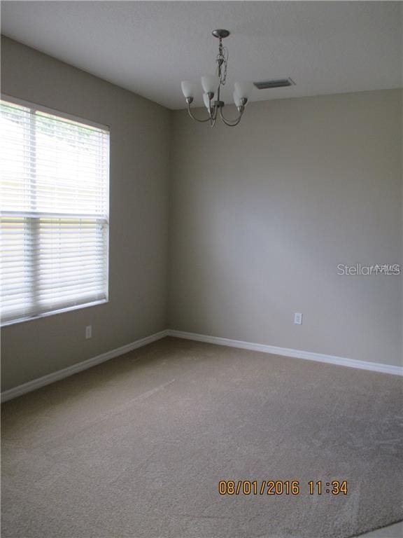 carpeted spare room featuring a notable chandelier