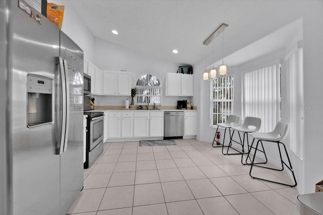 kitchen with light tile patterned floors, sink, appliances with stainless steel finishes, white cabinetry, and hanging light fixtures