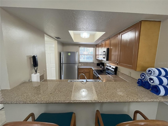 kitchen with appliances with stainless steel finishes, sink, a kitchen bar, kitchen peninsula, and a textured ceiling