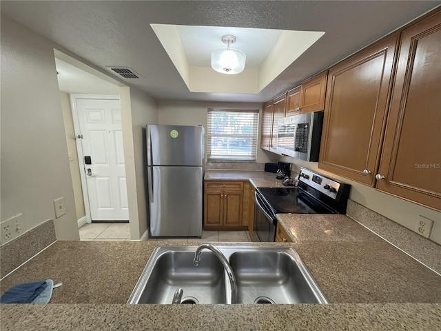 kitchen with a raised ceiling, light tile patterned flooring, appliances with stainless steel finishes, and sink