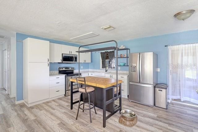 kitchen featuring white cabinetry, stainless steel appliances, a textured ceiling, and light wood-type flooring