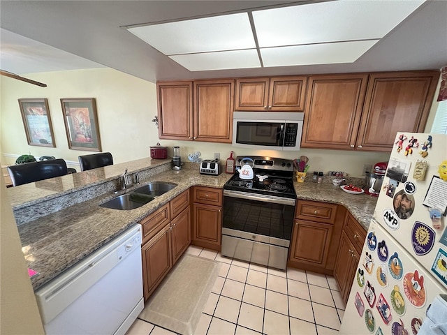 kitchen with appliances with stainless steel finishes, sink, light tile patterned floors, light stone counters, and kitchen peninsula