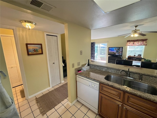 kitchen with dishwasher, sink, dark stone counters, light tile patterned floors, and ceiling fan