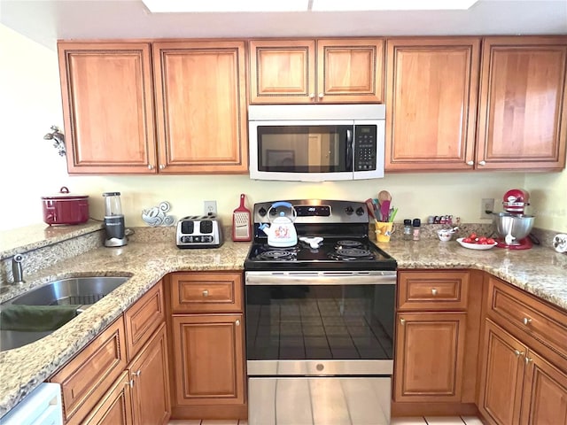 kitchen featuring light stone counters, appliances with stainless steel finishes, brown cabinetry, and a sink