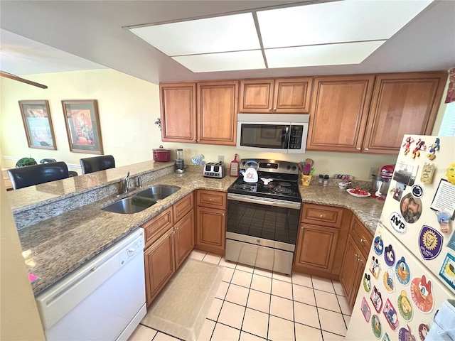kitchen featuring light tile patterned floors, stainless steel appliances, brown cabinetry, a sink, and a peninsula