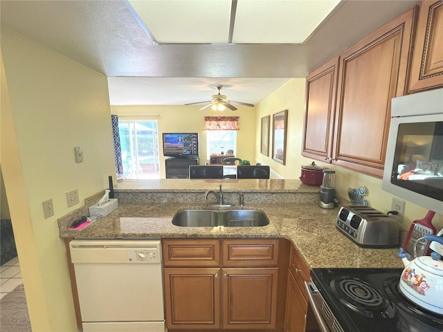 kitchen with ceiling fan, a sink, appliances with stainless steel finishes, brown cabinets, and light stone countertops