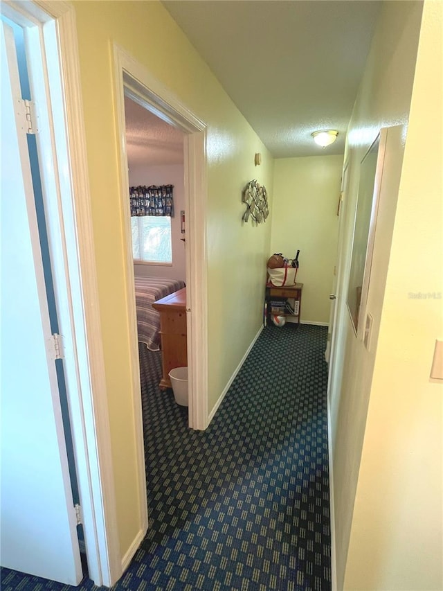 hallway featuring carpet, a textured ceiling, and baseboards