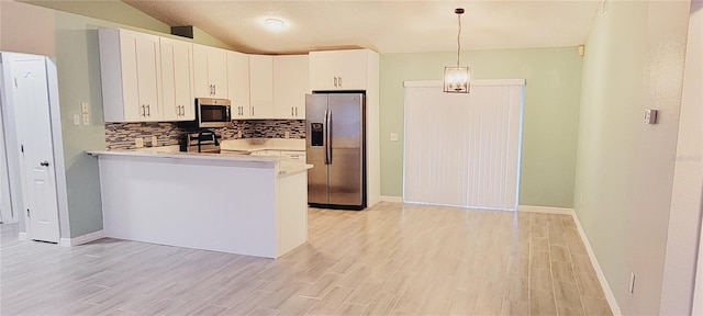 kitchen with appliances with stainless steel finishes, pendant lighting, white cabinetry, backsplash, and kitchen peninsula