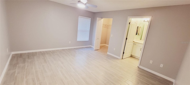 unfurnished bedroom with ensuite bath, a spacious closet, ceiling fan, and light wood-type flooring