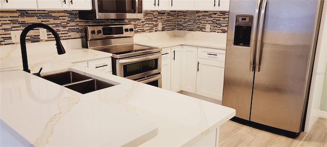 kitchen featuring stainless steel appliances, white cabinetry, light stone countertops, and decorative backsplash