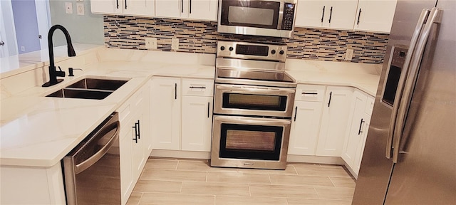 kitchen with stainless steel appliances, sink, white cabinets, and light stone counters