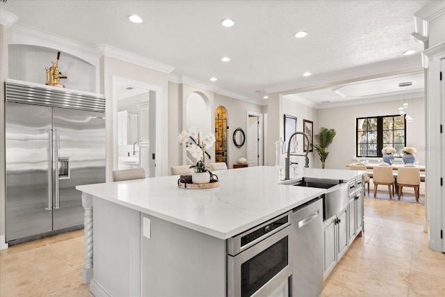 kitchen with an island with sink, sink, gray cabinetry, ornamental molding, and built in appliances