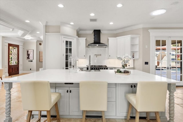 kitchen featuring wall chimney range hood, crown molding, a breakfast bar area, white cabinetry, and a large island with sink