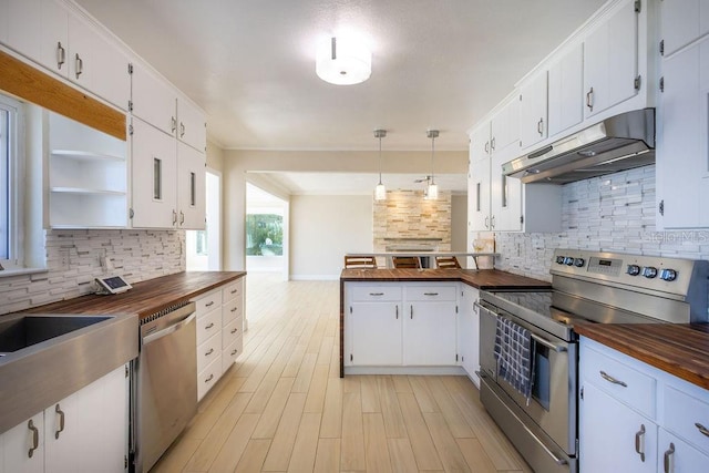 kitchen with appliances with stainless steel finishes, butcher block counters, white cabinets, and decorative light fixtures