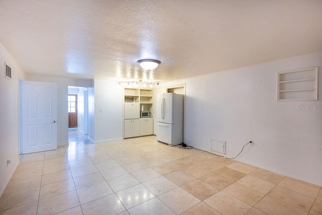 tiled spare room featuring built in shelves, rail lighting, and a textured ceiling