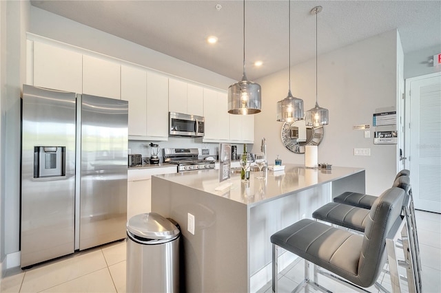 kitchen with appliances with stainless steel finishes, pendant lighting, white cabinets, and a kitchen bar