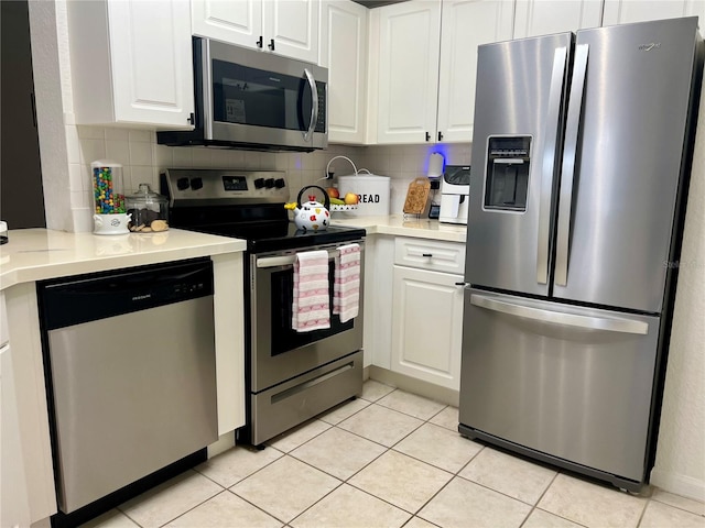 kitchen featuring stainless steel appliances, light tile patterned floors, white cabinets, and backsplash