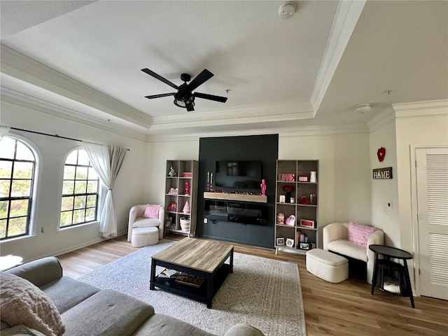 living room with a raised ceiling, crown molding, hardwood / wood-style flooring, and ceiling fan