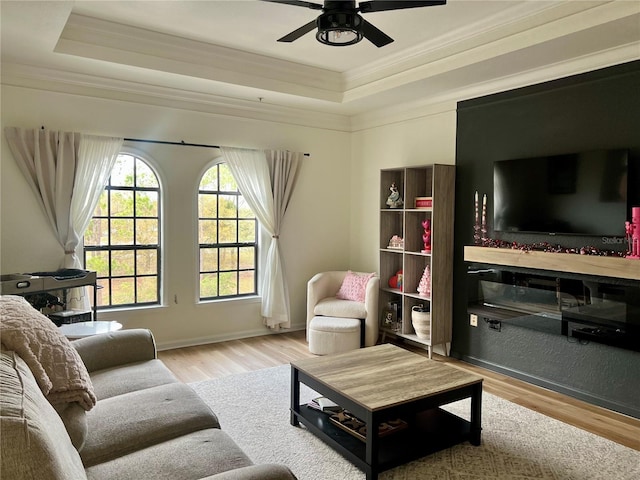 living room featuring crown molding, a tray ceiling, and light wood-type flooring