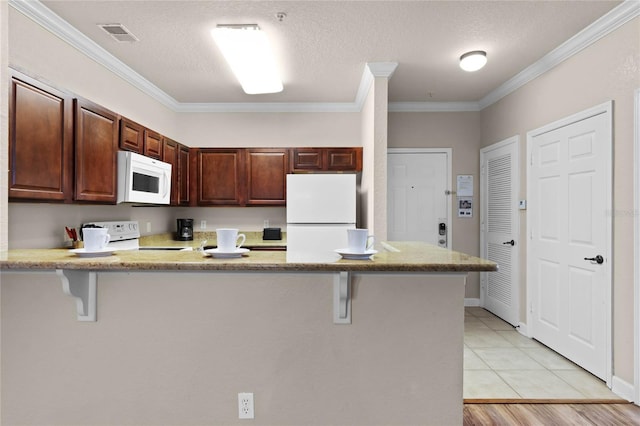 kitchen featuring a kitchen breakfast bar, ornamental molding, white appliances, and kitchen peninsula