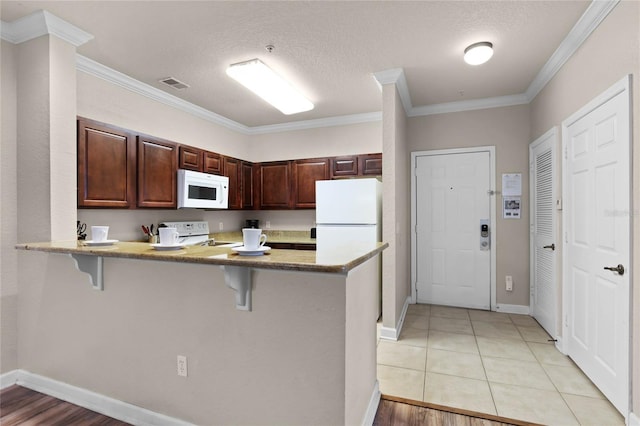 kitchen with light tile patterned flooring, a kitchen bar, ornamental molding, kitchen peninsula, and white appliances