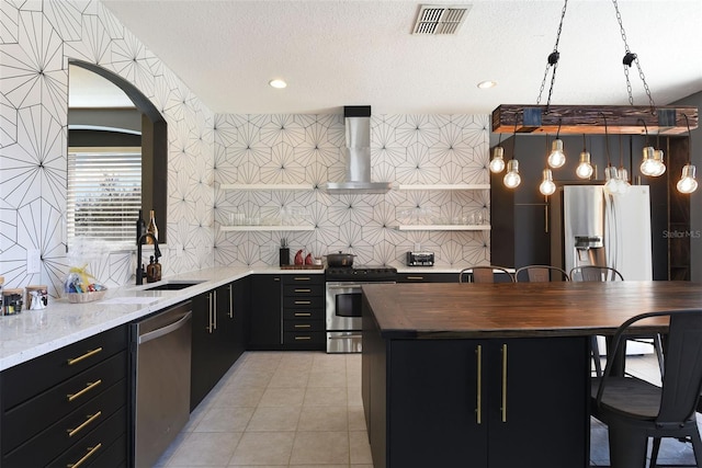 kitchen with a kitchen island, butcher block countertops, sink, stainless steel appliances, and wall chimney range hood