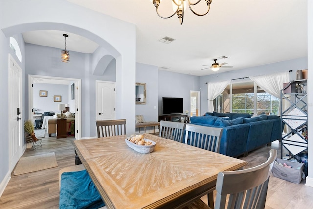 dining room with ceiling fan with notable chandelier and light wood-type flooring