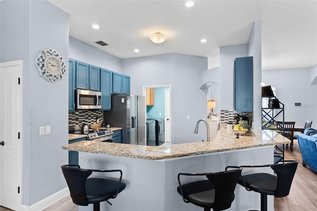 kitchen featuring blue cabinetry, appliances with stainless steel finishes, a kitchen breakfast bar, washing machine and clothes dryer, and kitchen peninsula