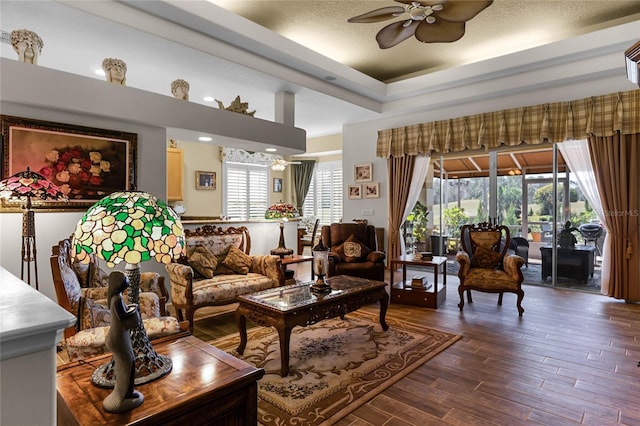 living room featuring a raised ceiling, ceiling fan, a textured ceiling, and dark hardwood / wood-style flooring