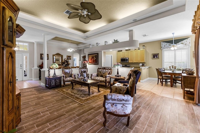 living room with ceiling fan, a raised ceiling, decorative columns, and a textured ceiling