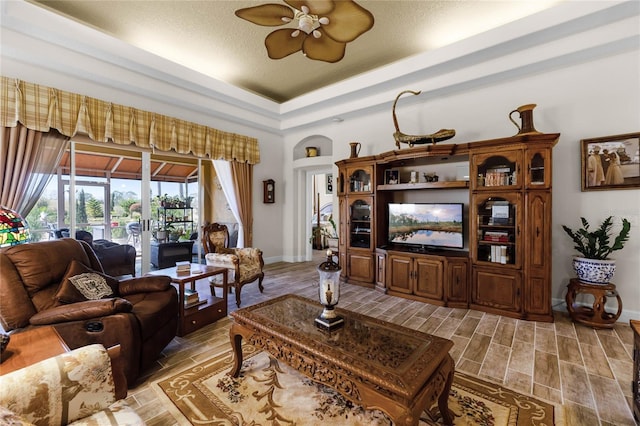 living room with a textured ceiling, a raised ceiling, and ceiling fan