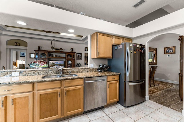 kitchen featuring appliances with stainless steel finishes, sink, light tile patterned floors, a raised ceiling, and light stone countertops