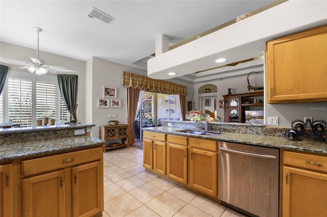 kitchen featuring sink, dark stone countertops, stainless steel dishwasher, light tile patterned floors, and ceiling fan