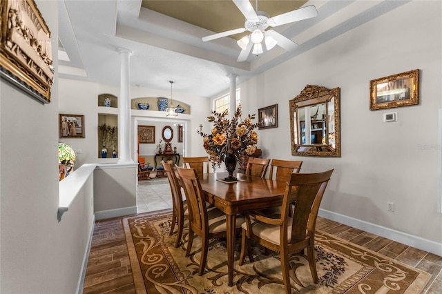 dining area featuring decorative columns, a raised ceiling, and hardwood / wood-style flooring