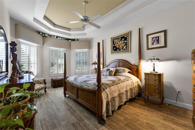 bedroom with a tray ceiling, wood-type flooring, a textured ceiling, and ceiling fan