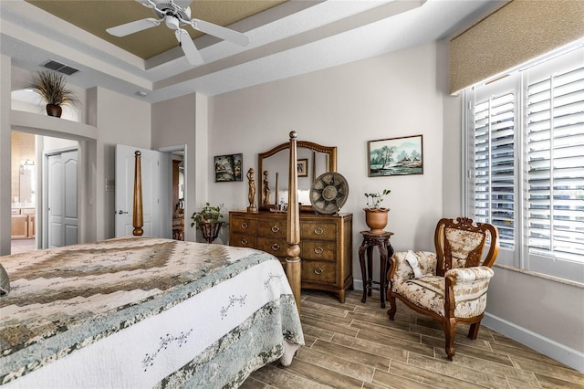 bedroom with ensuite bath, a raised ceiling, and ceiling fan