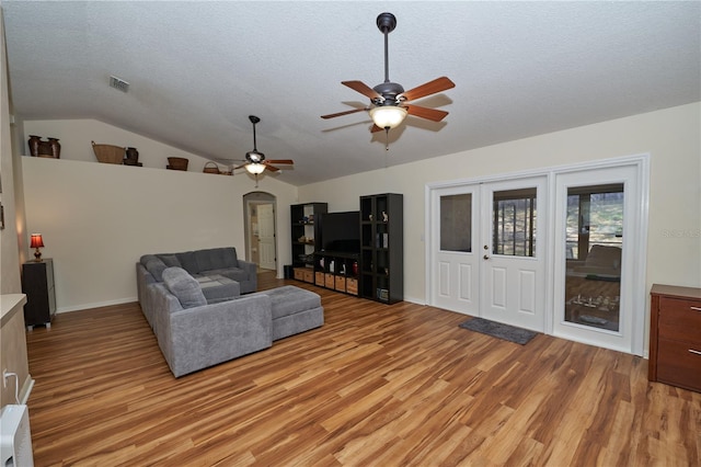 living room with lofted ceiling, a textured ceiling, ceiling fan, and light wood-type flooring