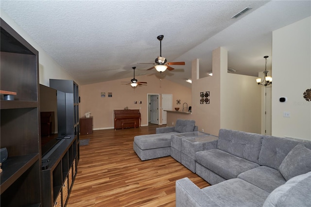 living room featuring lofted ceiling, ceiling fan with notable chandelier, a textured ceiling, and light hardwood / wood-style flooring