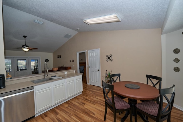 kitchen featuring sink, light hardwood / wood-style flooring, white cabinetry, vaulted ceiling, and stainless steel dishwasher